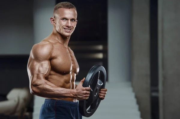 Caucasian power athletic man training pumping up biceps muscles. Strong bodybuilder with six pack, perfect abs, triceps, chest, shoulders in gym. Fitness and bodybuilding concept