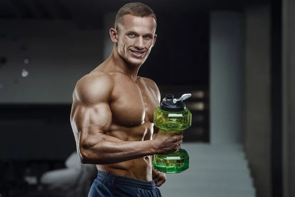 Fitness man in gym drinking water after workout. Fitness and bodybuilding healthy background. Caucasian man doing exercises in gym. Water bottle and supplements nutrition concept