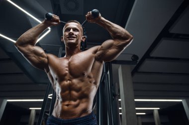 Beyaz tenli atletik adam triseps kaslarını çalıştırıyor. Güçlü vücut geliştirici, karın kasları, trisepsleri, göğsü ve omuzları var. Fitness ve vücut geliştirme konsepti