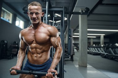 Beyaz tenli atletik adam kaslarını şişiriyor. Güçlü vücut geliştirici, karın kasları, trisepsleri, göğsü ve omuzları var. Fitness ve vücut geliştirme konsepti