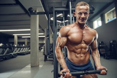 Beyaz tenli atletik adam kaslarını şişiriyor. Güçlü vücut geliştirici, karın kasları, trisepsleri, göğsü ve omuzları var. Fitness ve vücut geliştirme konsepti