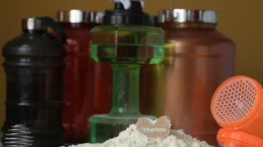 Protein tozu ve ölçüm kepçesi kavanozun üzerinde ve sallanan şişe arka planında. Vücut geliştirme, fitness ve spor salonu yaşam tarzı. Spor, sağlık ve beslenme konsepti