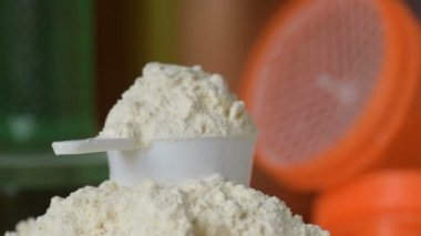 Protein tozu ve ölçüm kepçesi kavanozun üzerinde ve sallanan şişe arka planında. Vücut geliştirme, fitness ve spor salonu yaşam tarzı. Spor, sağlık ve beslenme konsepti