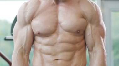 Beyaz tenli atletik adam kaslarını şişiriyor. Güçlü vücut geliştirici, karın kasları, trisepsleri, göğsü ve omuzları var. Fitness ve vücut geliştirme konsepti