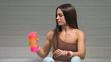 Spor salonunda spor salonunda spor salonundaki turuncu ve pembe karıştırıcıdan su içen kadın. Egzersiz yapan beyaz bir kız. Fitness, vücut geliştirme ve sağlık hizmeti kavramı.