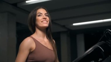 Spor salonunda koşan genç bir kadın dışarı bakıyor. Kardiyoda gülümseyen heyecanlı kız. Kafkasyalı spor salonunda kaslarını şişiren hoş bir kadın. Sağlık hizmetleri kavramı