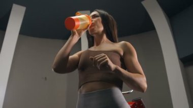Spor salonunda spor salonunda spor salonundaki turuncu ve pembe karıştırıcıdan su içen kadın. Egzersiz yapan beyaz bir kız. Fitness, vücut geliştirme ve sağlık hizmeti kavramı.