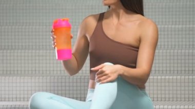 Spor salonunda spor salonunda spor salonundaki turuncu ve pembe karıştırıcıdan su içen kadın. Egzersiz yapan beyaz bir kız. Fitness, vücut geliştirme ve sağlık hizmeti kavramı.
