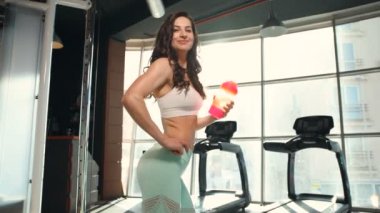 Spor salonunda spor salonunda spor salonundaki turuncu ve pembe karıştırıcıdan su içen kadın. Egzersiz yapan beyaz bir kız. Fitness, vücut geliştirme ve sağlık hizmeti kavramı. 