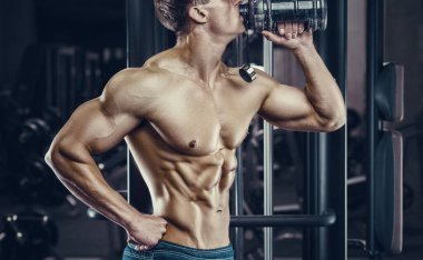 Vücut geliştirici güçlü atletik sert adam vücut geliştirme egzersizi ve vücut geliştirme konsepti tasarımından sonra su içiyor. Kas geliştiren sporcular spor salonunda çıplak gövde egzersizleri yapıyor.