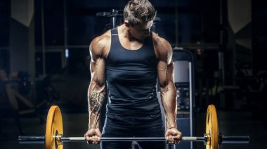 Yakışıklı, formda, kaslı, beyaz bir adam spor salonunda antrenman yapıyor. Kilo alıyor, kaslarını şişiriyor, fitness ve vücut geliştirme sporları yapıyor.