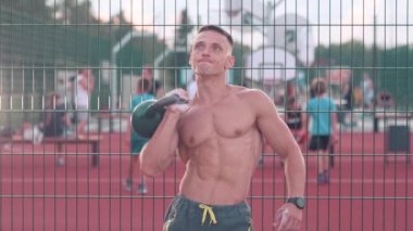 Kaslı atletik genç adam çitin yanındaki spor bahçesinde kettlebell egzersizi yapıyor. Sağlık hizmeti kavramı 
