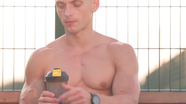 Ein Muskulöser Athletischer Junger Mann Sitzt Auf Einer Bank Trinkt — Stockvideo