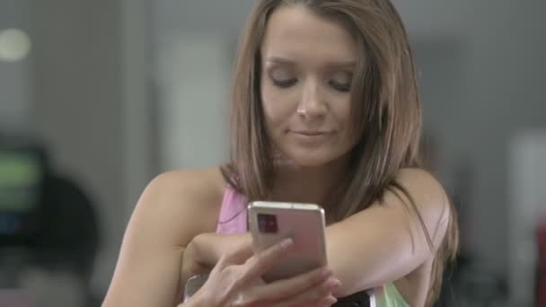 健身房里的年轻女子看着手机笑得很兴奋 白种人健身女孩在锻炼期间 体育和保健概念 — 图库视频影像