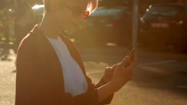 Şehir caddesinde akıllı telefondan fotoğraf çeken genç bir kız. Kırmızı paltolu ve kırmızı yuvarlak gözlüklü havalı hippi cumhuriyetçi öğrenci