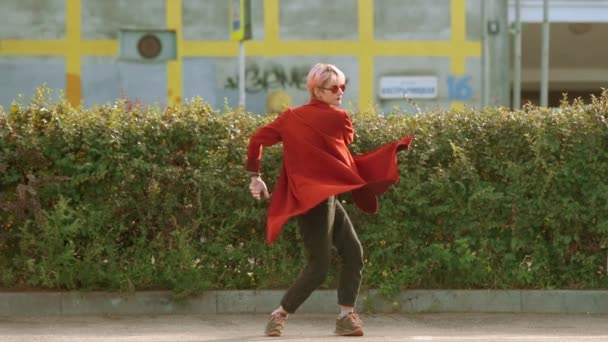 クールなヒップスターオークションアジアの学生の女の子身に着けています赤コートと赤丸メガネダンスで街の通り — ストック動画