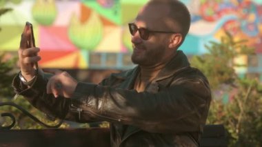 Genç adam kafenin dışındaki akıllı telefondan fotoğraf çekiyor. Deri ceketli yakışıklı beyaz adam. 