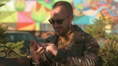 Şehir caddesindeki bir akıllı telefondan mesaj yazan genç bir adam. Deri ceketli yakışıklı beyaz adam. 