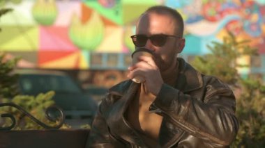 Genç bir adam kafedeki kağıt bardaktan kahve içiyor. Deri ceketli yakışıklı beyaz adam. 