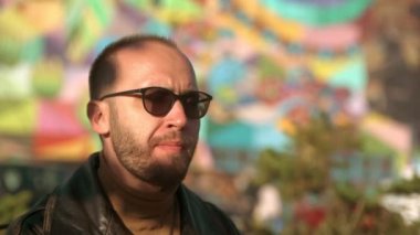 Genç adam kafede açık havada sosisli yiyor. Deri ceketli yakışıklı beyaz adam. 