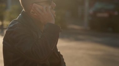 Genç adam şehir caddesinde bir cep telefonundan konuşuyor. Deri ceketli yakışıklı beyaz adam. 