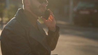 Genç adam şehir caddesinde bir cep telefonundan konuşuyor. Deri ceketli yakışıklı beyaz adam. 