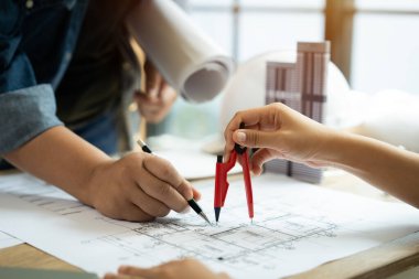 İki kişi kırmızı cetvelli bir kağıt parçasına resim çiziyor. Birinin elinde kalem, diğerinin elinde kırmızı bir cetvel var. Birlikte bir proje üzerinde çalışıyorlar.