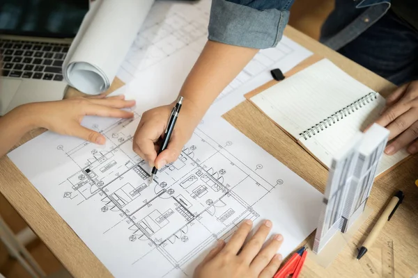 Bir adam ve bir kadın bir binanın çizimi üzerinde çalışıyorlar. Kadın çizime bakarken, adam binayı çizmek için bir kalem kullanıyor. Sahne odaklı ve işbirlikçi.