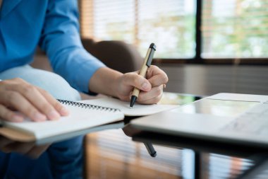 Bir kadın kalemle deftere yazı yazıyor. Önünde bir dizüstü bilgisayarla bir masada oturuyor. Sahne onun bir proje ya da ödev üzerinde çalıştığını ya da çalıştığını gösteriyor.