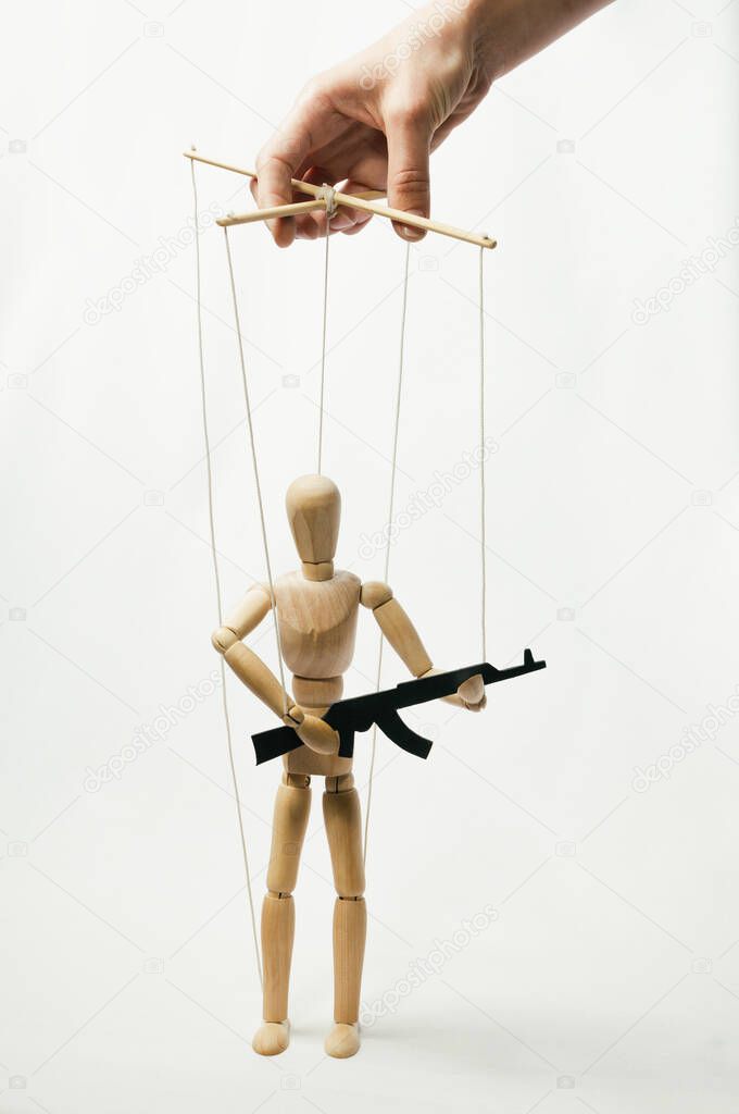 Marionette on the strings with rifle in the human hand. Concept of control.