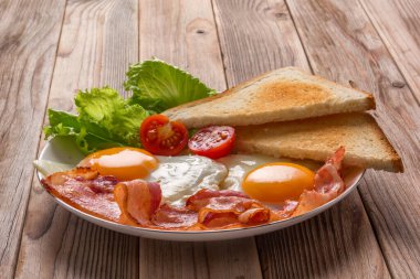 Beyaz tabak yumurta, domuz pastırması, tost ve sebzeler ahşap masada. Kapatın. Yumuşak odaklanma. Boşluğu kopyala