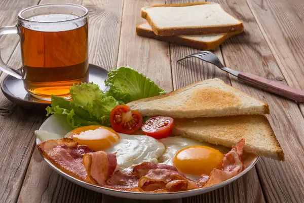 White Plate Fried Eggs Bacon Toasts Vegetables Wooden Table Glass — Stock Photo, Image