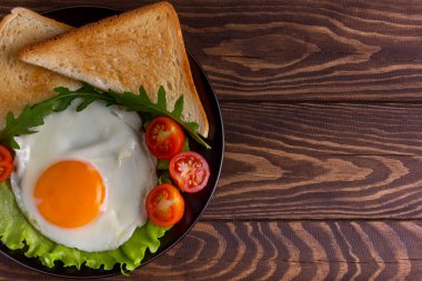 Domatesli sahanda yumurta, salata, roka ve sade ahşap arka planda üçgen tost, sağ fotokopi alanı. Kapat.