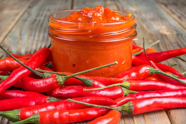 Ahşap zemin üzerinde acı kırmızı biberle çevrili cam bir Harissa kavanozunun yakın görüntüsü. Yumuşak odak.
