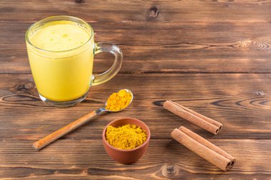 Tahta zemin üzerinde zerdeçal, tarçın, tahta kaşık ve bal olan bir fincan altın sütün görüntüsü. Yumuşak odak.