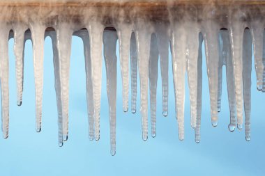 Buz saçaklarından mavi bir zemine düşen su damlası.