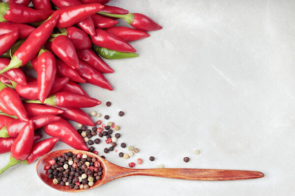 Top view of chili pepper and wooden spoon with red, black, white peppers on a gray concrete background. With copy space.