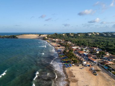 Arka planda küçük bir kasaba olan bir sahil. Su sakin ve gökyüzü berrak.