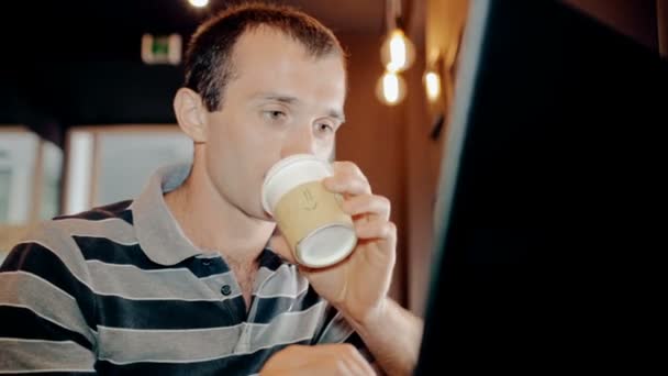 Чоловік працює на комп'ютері і п'є каву в кафе — стокове відео