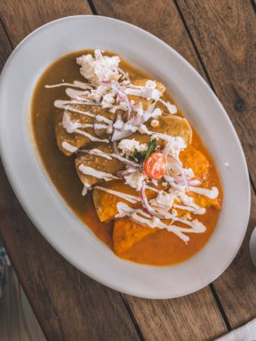 Geleneksel Meksika enchilada soslu, kremalı, peynirli ve kırmızı soğanlı Holbox, Meksika 'da ahşap masada servis ediliyor.