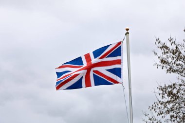 Açık hava sahnesinde doğal olarak rüzgarda dalgalanan Birleşik Krallık bayrağı, hareket, renk ve ulusal kimliği gösteriyor