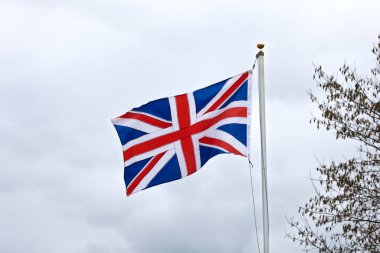 Açık hava sahnesinde doğal olarak rüzgarda dalgalanan Birleşik Krallık bayrağı, hareket, renk ve ulusal kimliği gösteriyor