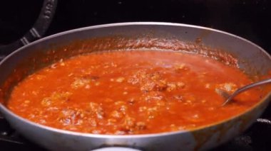 Tavada makarna sosu pişiyor, sucuk pişiriyor.