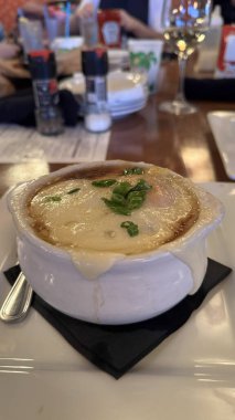 Sıcak ortam aydınlatmalı sıcak bir restoranda sunulan, otlarla süslenmiş, iştah açıcı bir kase fırında peynir çorbası. Yüksek kalite fotoğraf