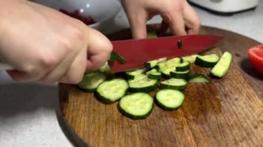 A close-up of hands slicing cucumbers on a wooden cutting board.