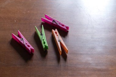 Dört renkli plastik mandal, ikisi pembe, biri yeşil, biri turuncu, koyu ahşap bir masaya saçılmış, sıcak ve basit bir sahne yaratıyor.