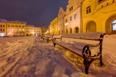 Pelhrimov 2025 'teki Masaryk Meydanı' nda karla kaplı bankların görüntüsü, sokak ışıkları, temiz kar örtüsü, tarihi evler.