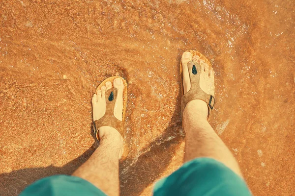 Mens feet in sandals on the beach.