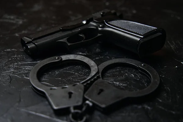 Gun and handcuffs on black textured table. — Stock Photo, Image