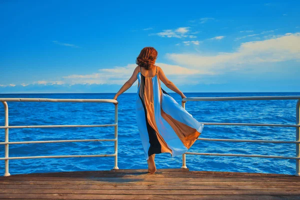 Pretty girl in flowing long dress stands on edge of pier. — Stock Photo, Image